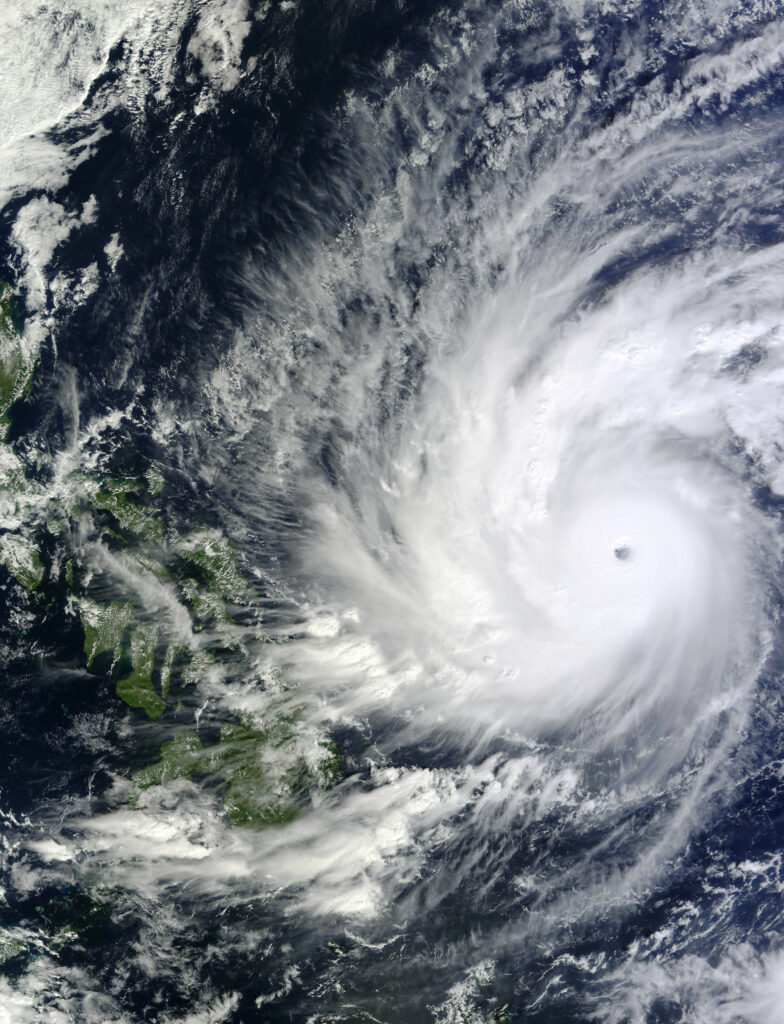 Aerial view of massive hurricane with swirling clouds and eye over Earth’s blue ocean and green land Wallpaper
