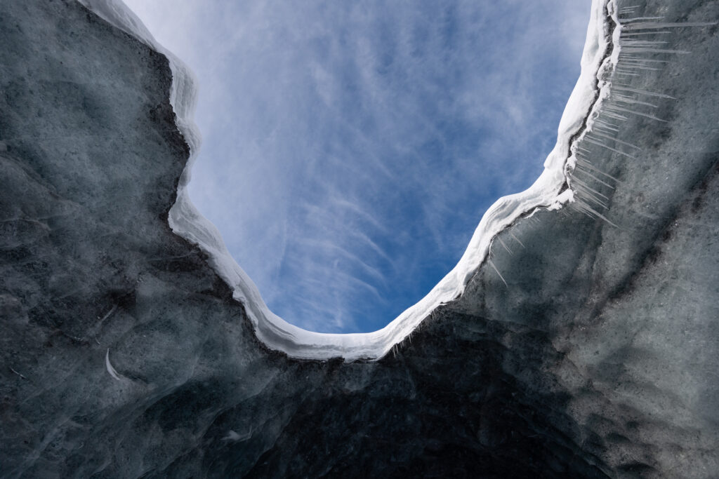 Inside ice cave view with vivid blue sky textured icy walls and delicate icicles wallpaper background