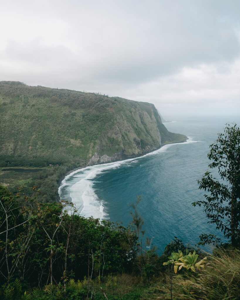 Breathtaking island wallpaper with lush trees cliffs rolling waves and deep blue sea under clouds