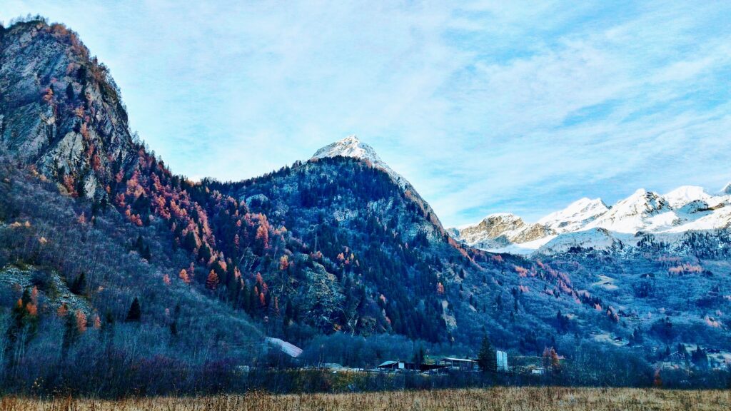 Italian mountain landscape with snowy peaks autumn forests and alpine village under blue sky Wallpaper