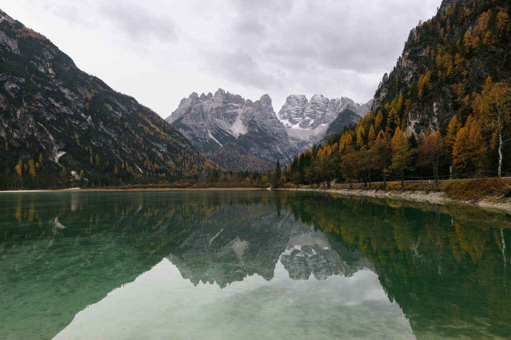 Mountain landscape wallpaper with autumn trees reflecting in a serene lake under cloudy sky