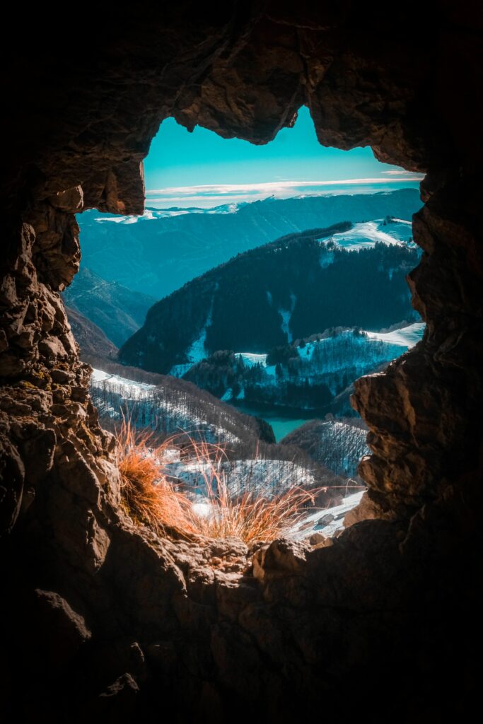 Mountain landscape viewed through cave opening with snow-capped peaks and bright blue sky wallpaper