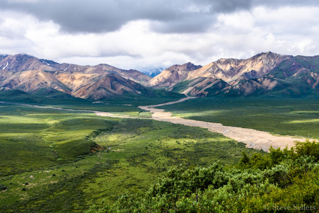 Breathtaking mountain landscape with rugged peaks winding valley vibrant green fields under moody sky Wallpaper