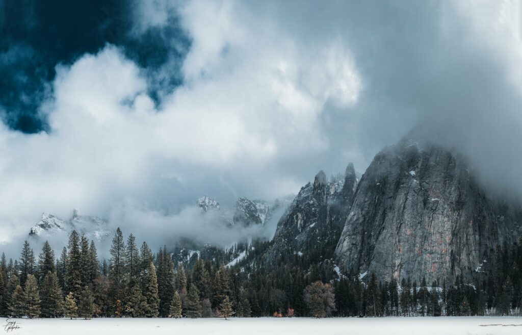 Breathtaking snowy mountain landscape with evergreen trees and dramatic clouds in HD wallpaper