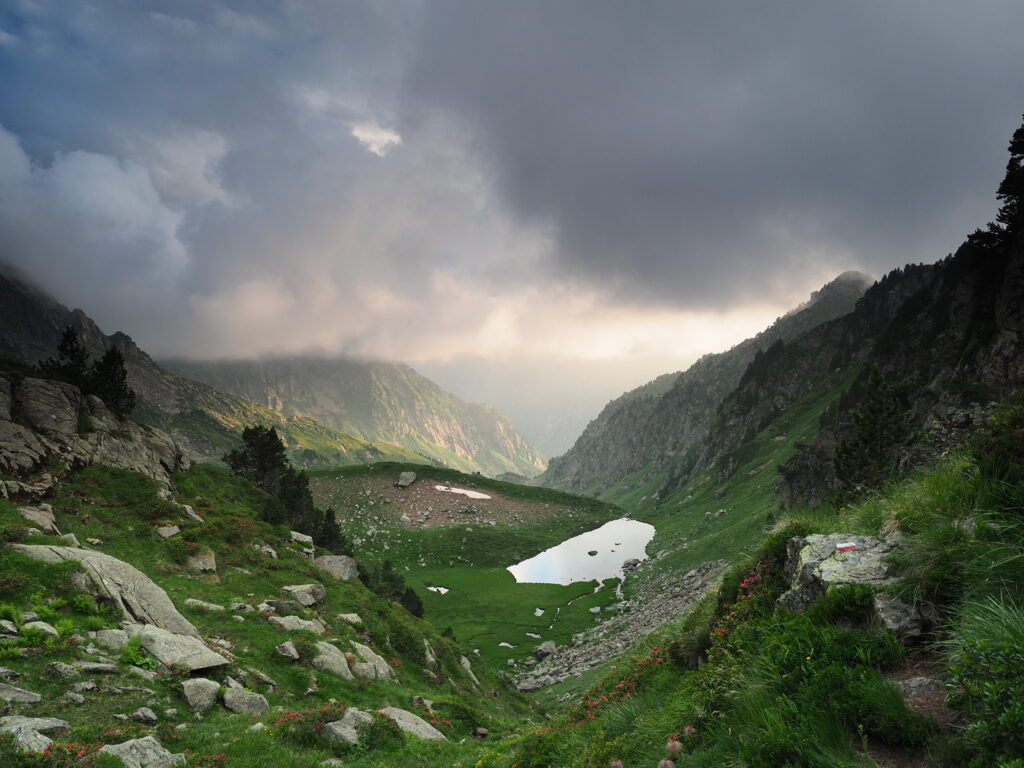 Breathtaking mountain landscape with lush green valley serene reflective pond dramatic clouds Wallpaper