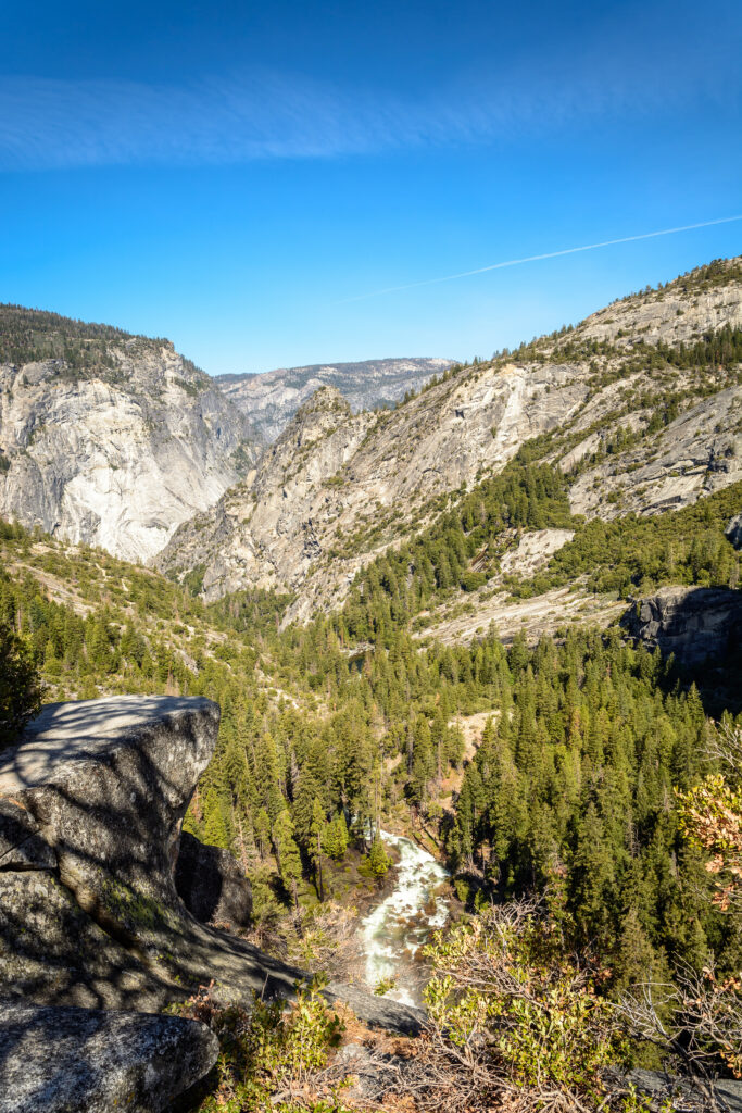 Breathtaking mountain landscape with rugged cliffs dense pines and winding river under blue sky Wallpaper