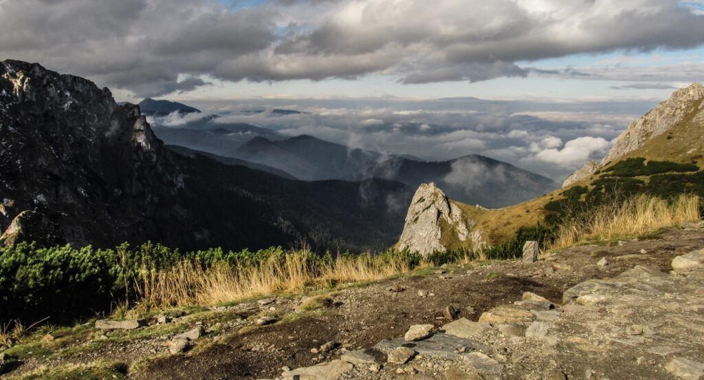 Breathtaking mountain landscape with rugged rocks golden grass and misty peaks under cloudy sky Wallpaper