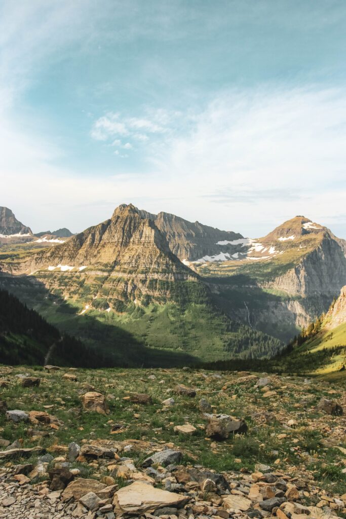 Breathtaking mountain landscape with rocky foreground lush green slopes and snowy peaks under clouds Wallpaper