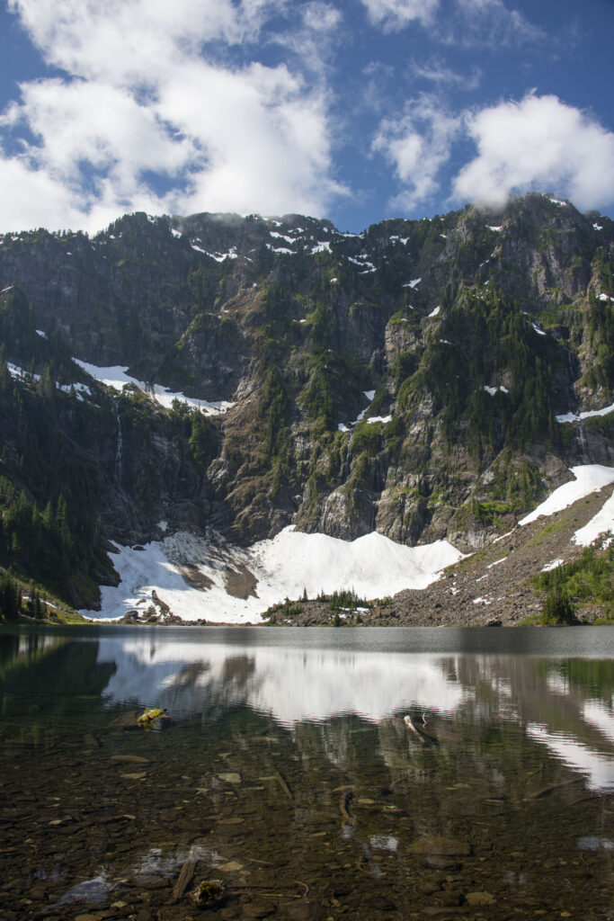 Breathtaking alpine mountain landscape with snowy peaks reflected in a clear river and lush greenery Wallpaper