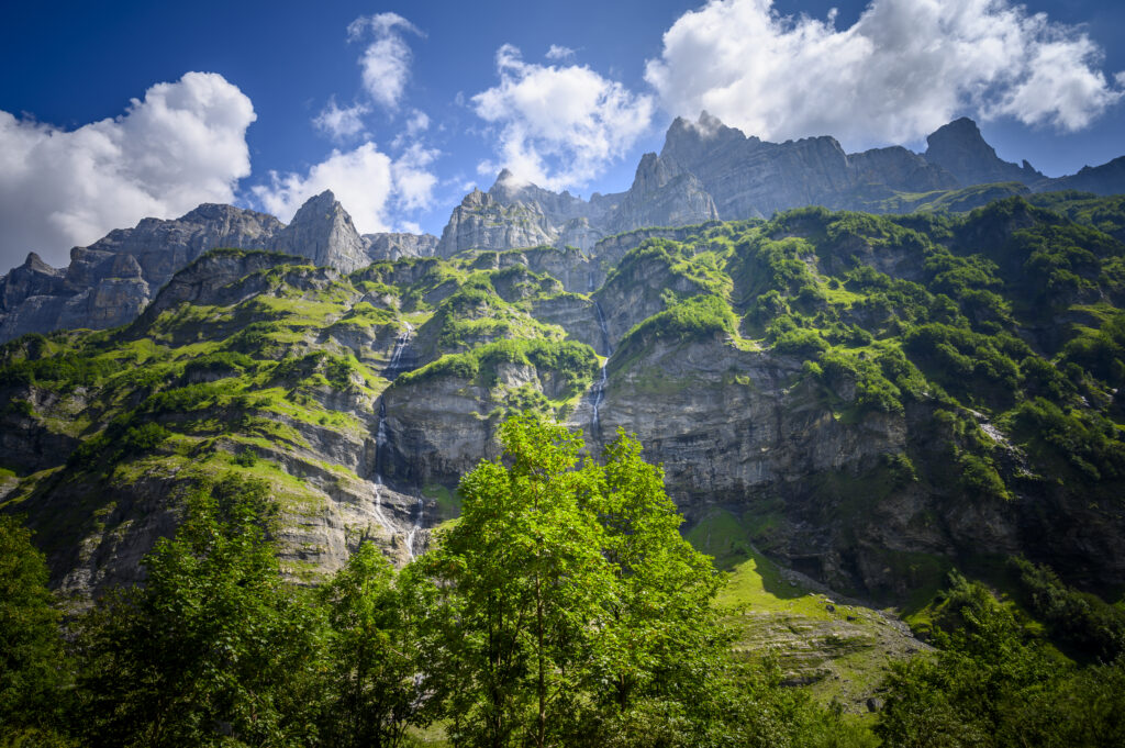 Breathtaking mountain landscape with rugged rocks waterfall green bushes and bright blue sky Wallpaper