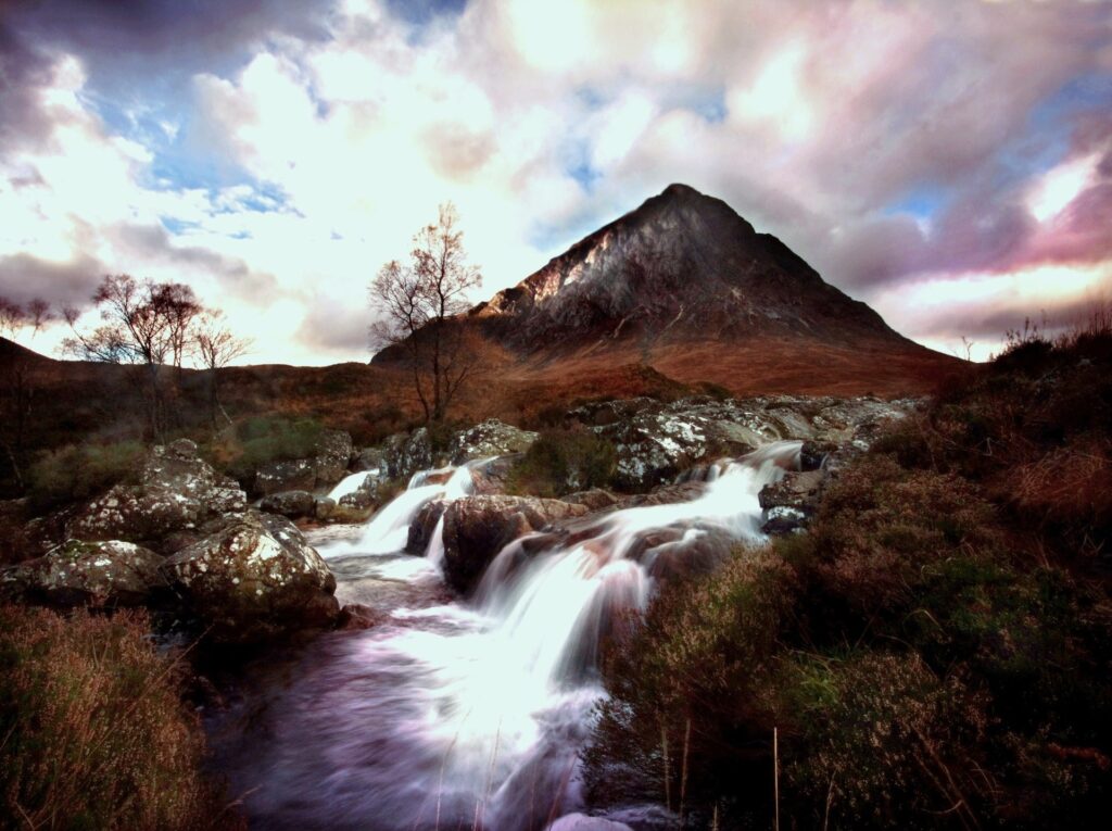 Mountain river flowing over mossy rocks with towering peak and colorful dramatic sky wallpaper