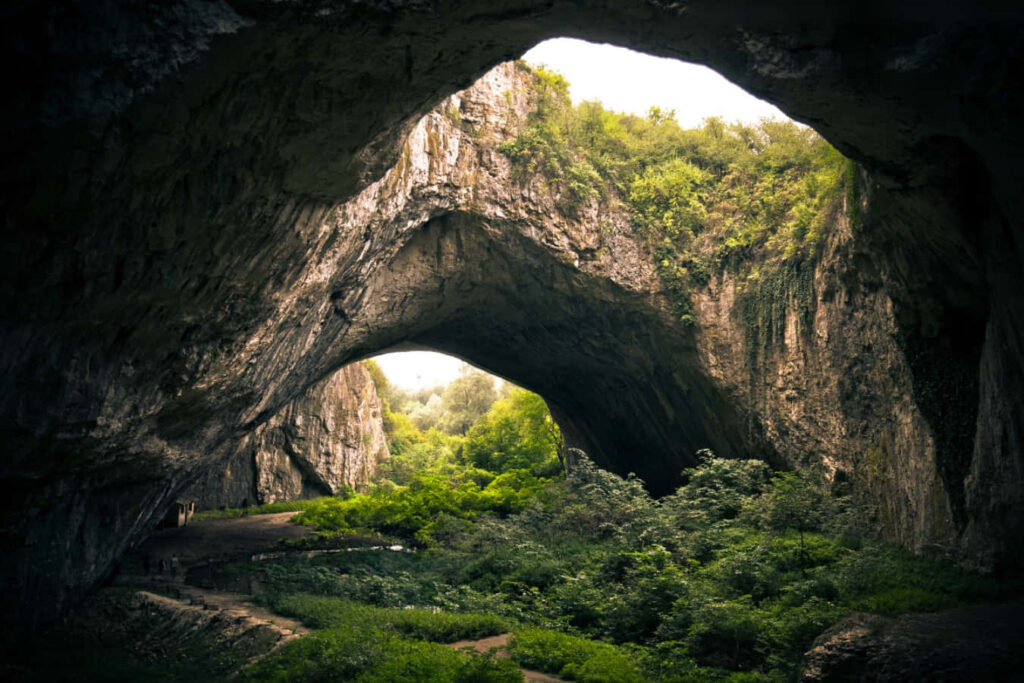 Captivating Mystic Cave View with Lush Landscape and Sunlit Shadows Wallpaper