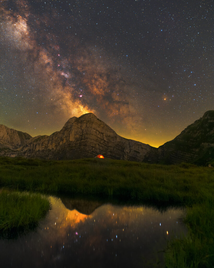 Night wallpaper with rocky mountain lush grass serene pond reflecting vibrant Milky Way stars