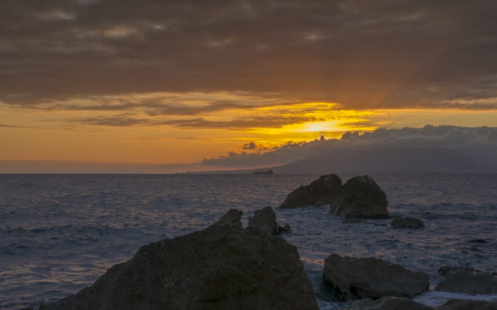 Sunset over ocean with golden sky rocks and gentle waves coastal wallpaper background serene