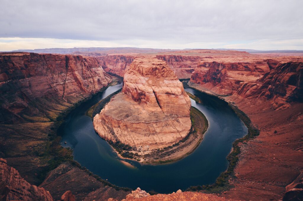 Panoramic canyon landscape with red rock formations and winding river under muted sky wallpaper