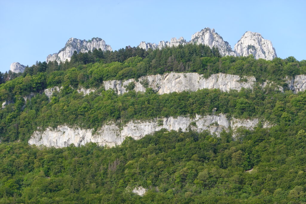 Breathtaking landscape with rugged cliffs above dense green forest under clear blue sky wallpaper