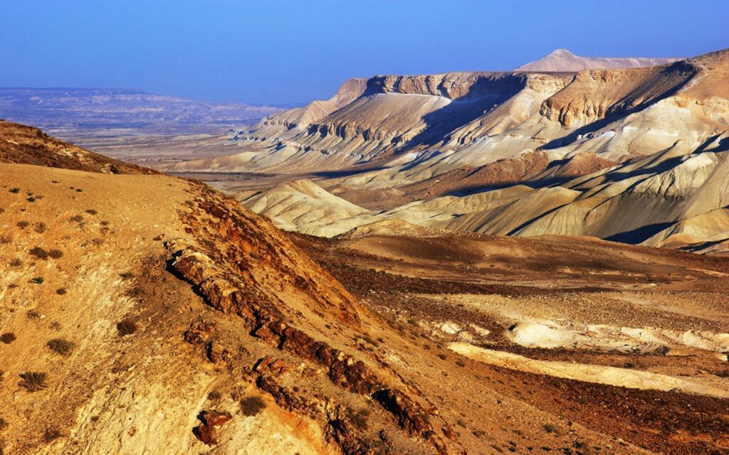 Rugged mountains with layered rocks sandy slopes and grass under clear blue sky wallpaper background