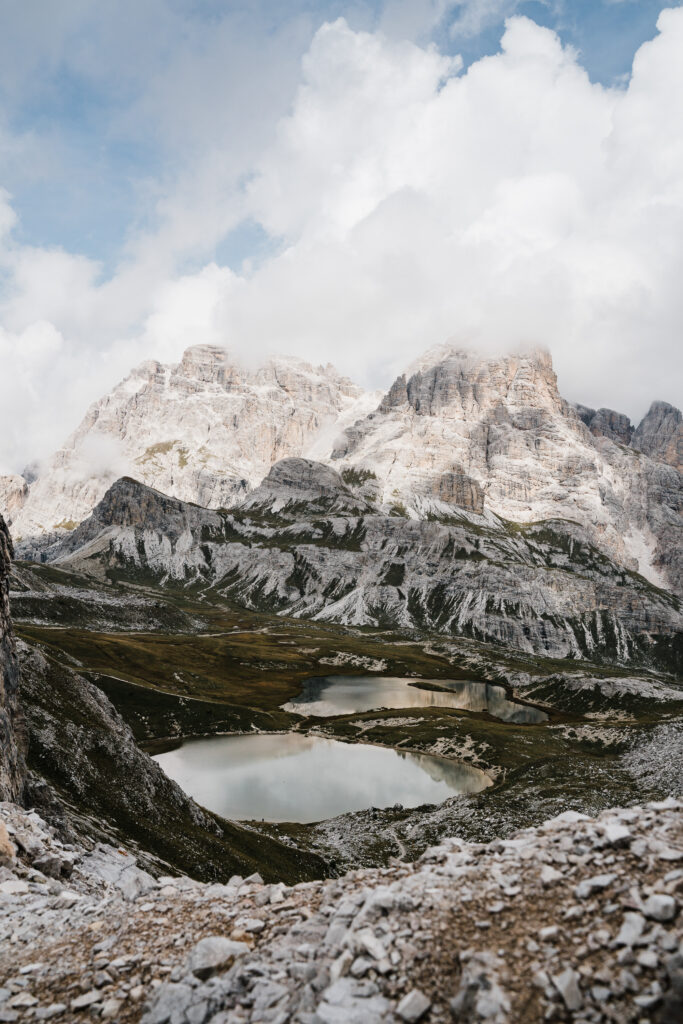 Rugged mountain landscape with dramatic clouds and serene lakes in earthy gray and green tones Wallpaper