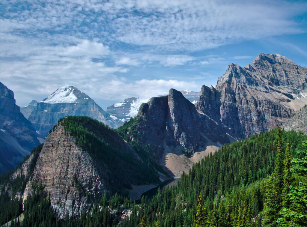Rugged mountains with snowy peaks over dense evergreen forest under bright blue sky wallpaper