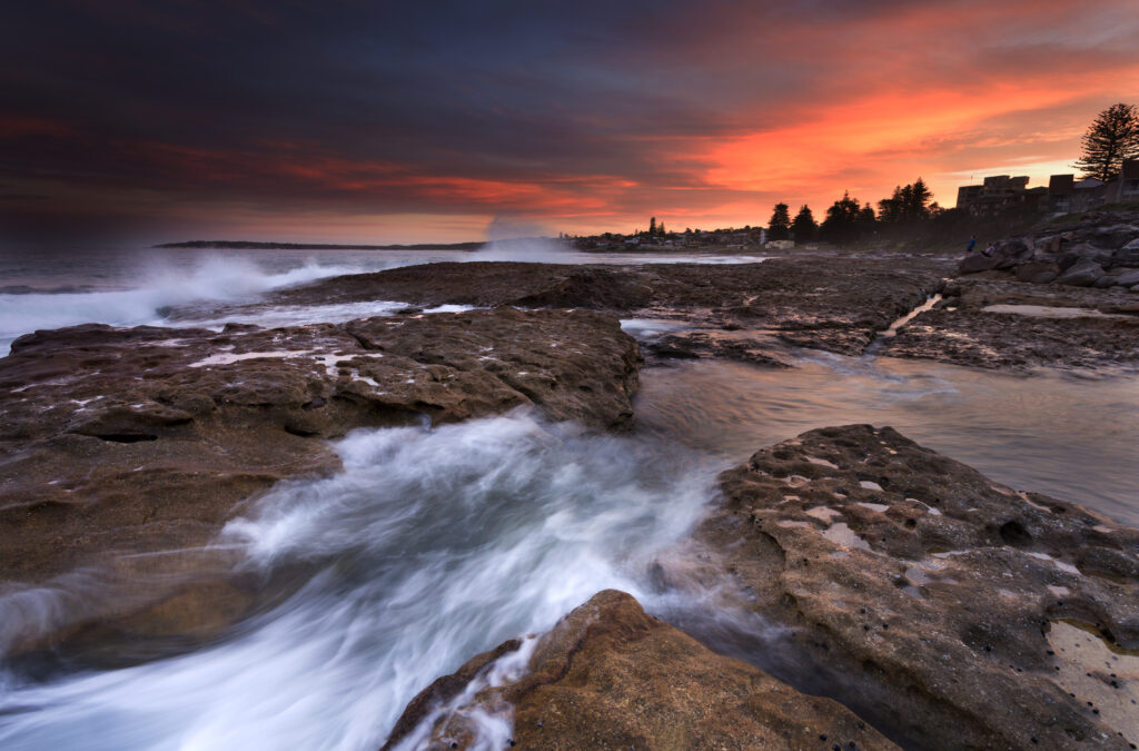 Seascape wallpaper with rugged rocks and vibrant sunset sky over powerful surf on shoreline