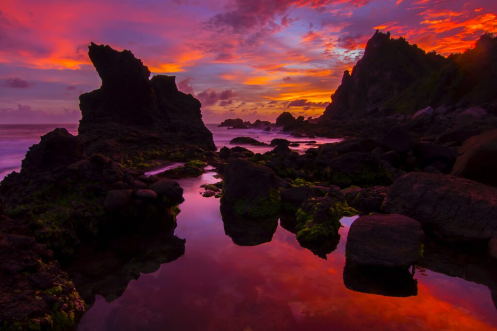 Sunset seascape with rugged rocks tidal pools purple orange pink sky reflecting calm water Wallpaper
