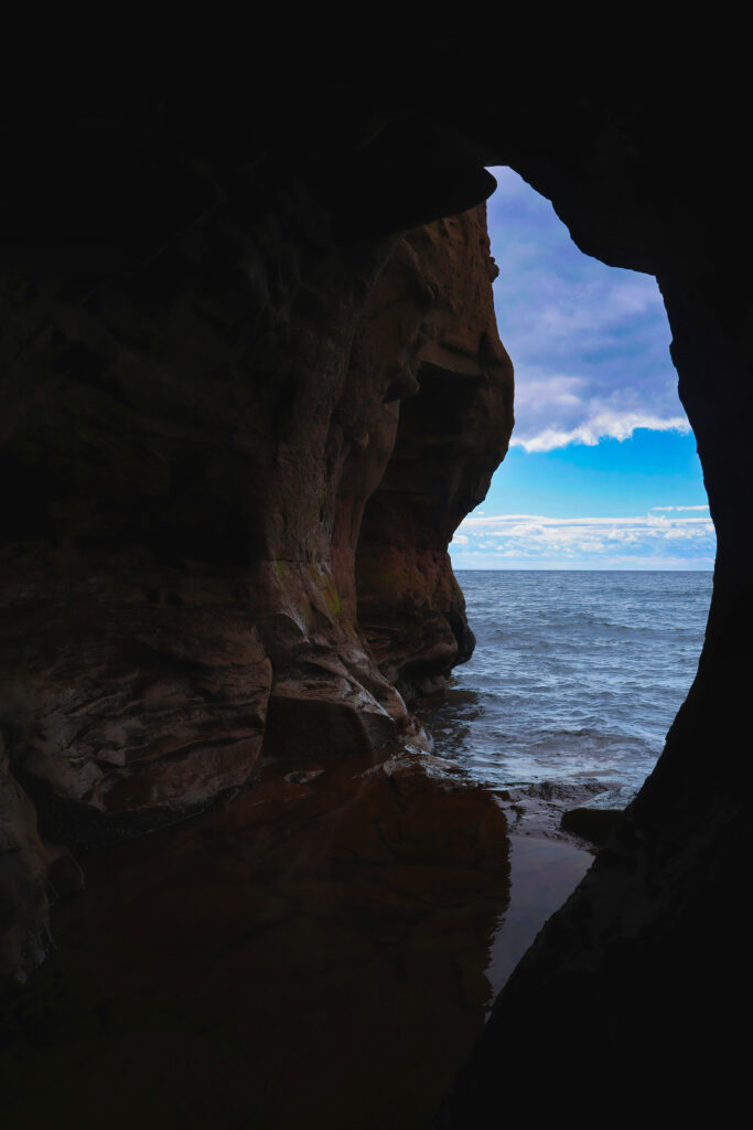 Ocean view from dark seaside cave with deep blue water and soft cloudy sky background Wallpaper