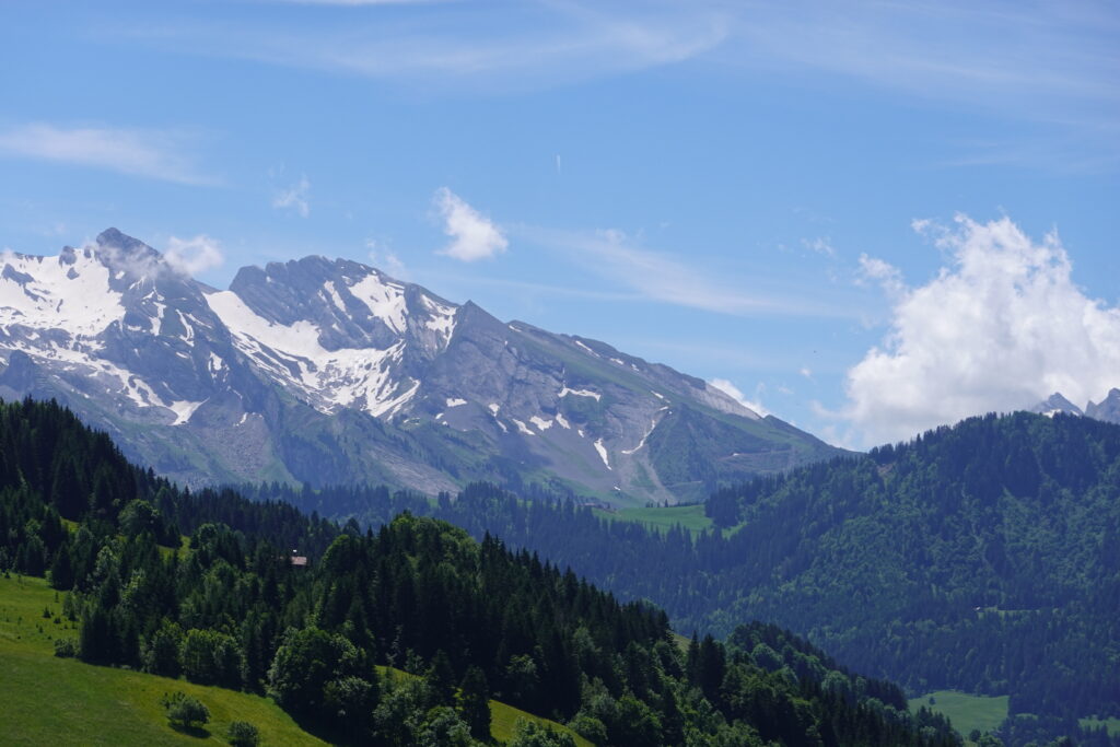 Snow-capped mountains with green forests and rolling hills under a bright blue sky wallpaper