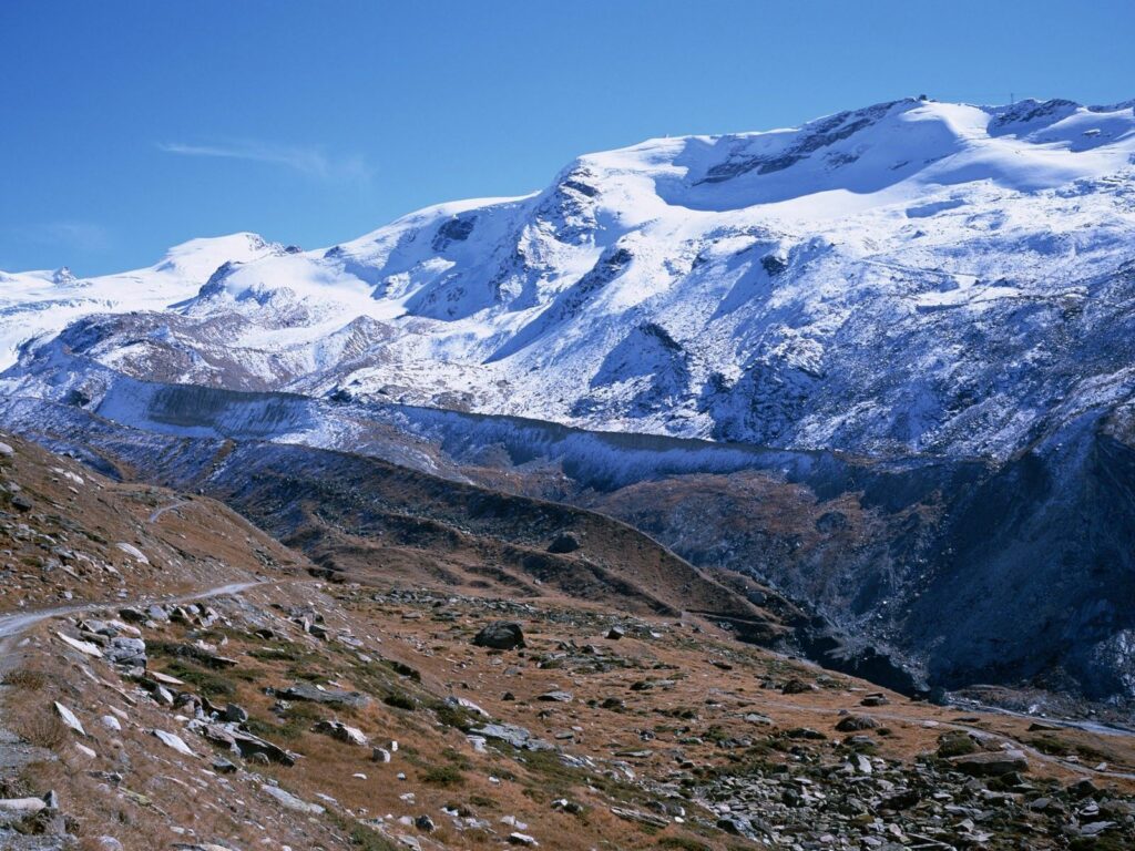 Snow-capped rugged mountains with winding trail foreground blue sky scenic mountain landscape wallpaper