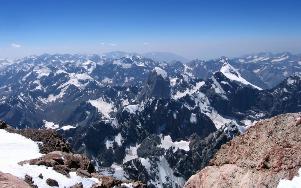 Vast mountain range with rugged ridges snow-capped peaks and dramatic gorges under blue sky Wallpaper