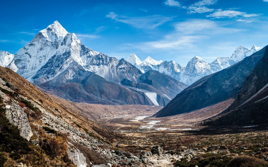 Snow-capped mountain peaks with rugged slopes and winding valley under clear blue sky wallpaper background