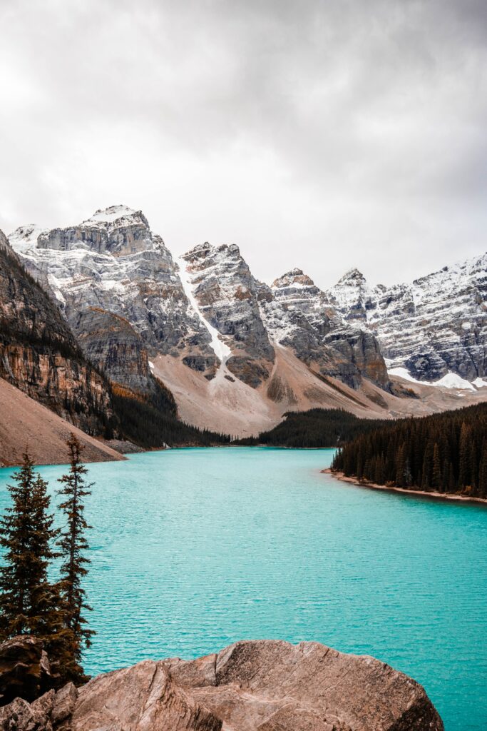 Snow-capped mountains above turquoise lake surrounded by dense forest and rocky outcrops wallpaper