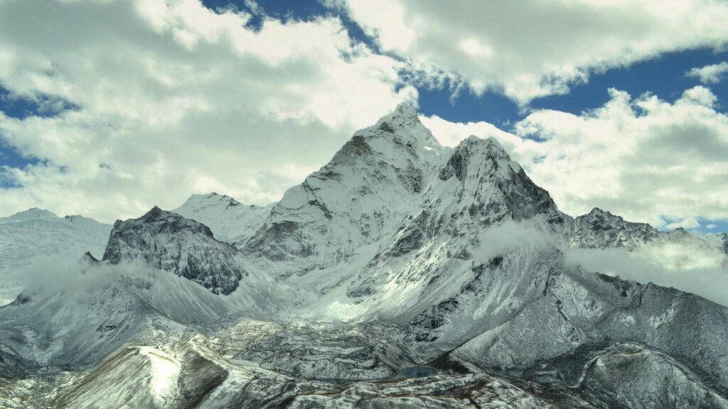 Snow-capped mountains under dramatic sky with fluffy clouds natural light highlights peaks Wallpaper