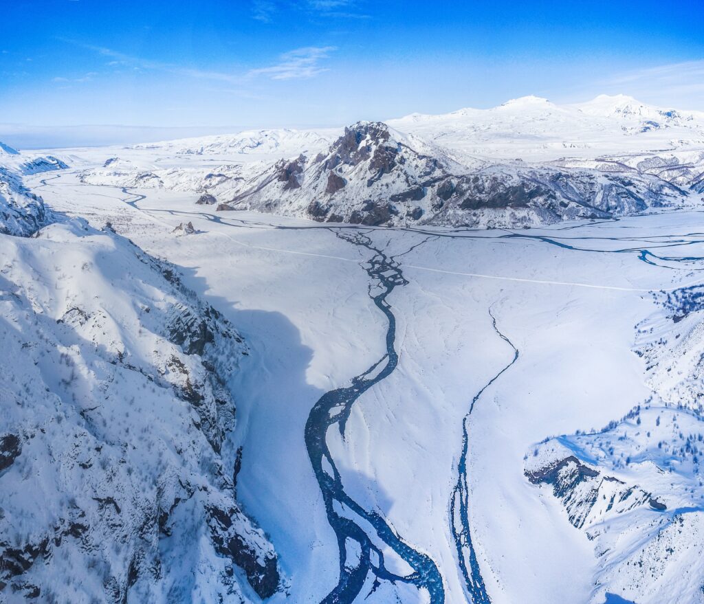 Aerial view of snow-covered mountains frozen valleys and winding streams under blue sky winter wallpaper