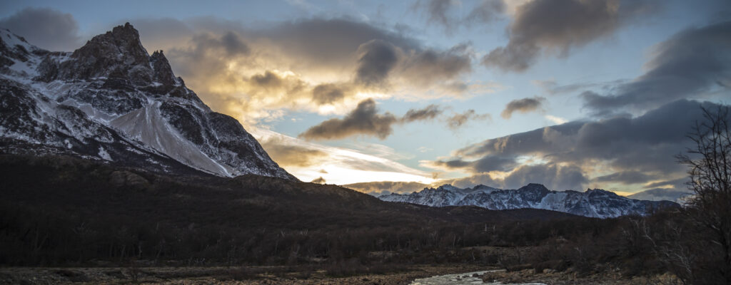 Dramatic snowy mountain peak with rugged trees and vibrant sunset sky natural landscape wallpaper