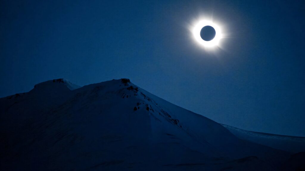 Solar eclipse over snow-capped mountains with deep blue hues and serene natural landscape wallpaper