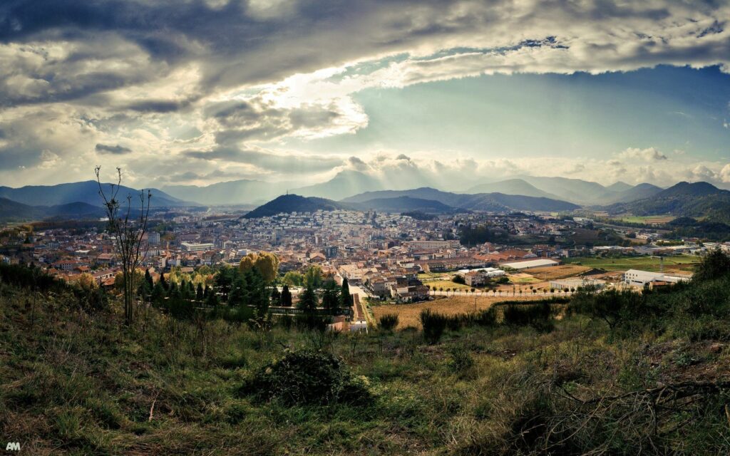 Breathtaking Spanish landscape with rolling hills vibrant valley town and dramatic sunlight clouds Wallpaper