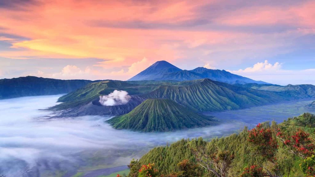 Sunrise over smoking Mount Bromo volcano in Indonesia with mist and Mount Semeru peak background Wallpaper