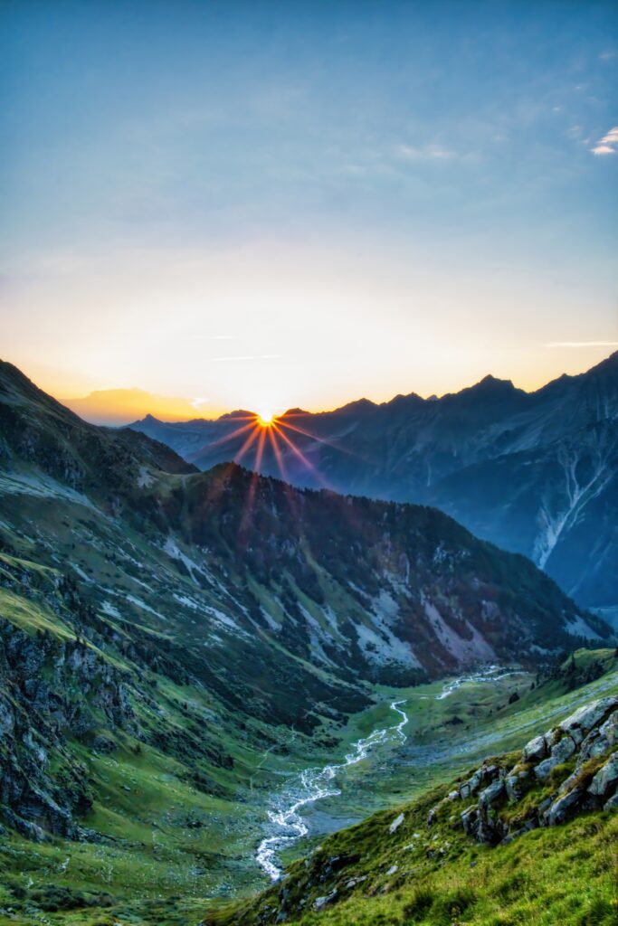 Sunrise over rugged mountains winding river lush green valley clear blue sky wallpaper background