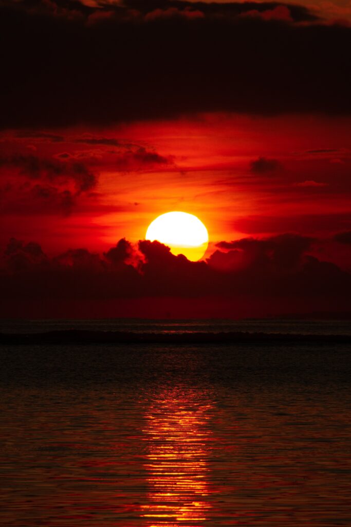 Vibrant sunset over calm sea with glowing sun and dramatic red orange clouds wallpaper background