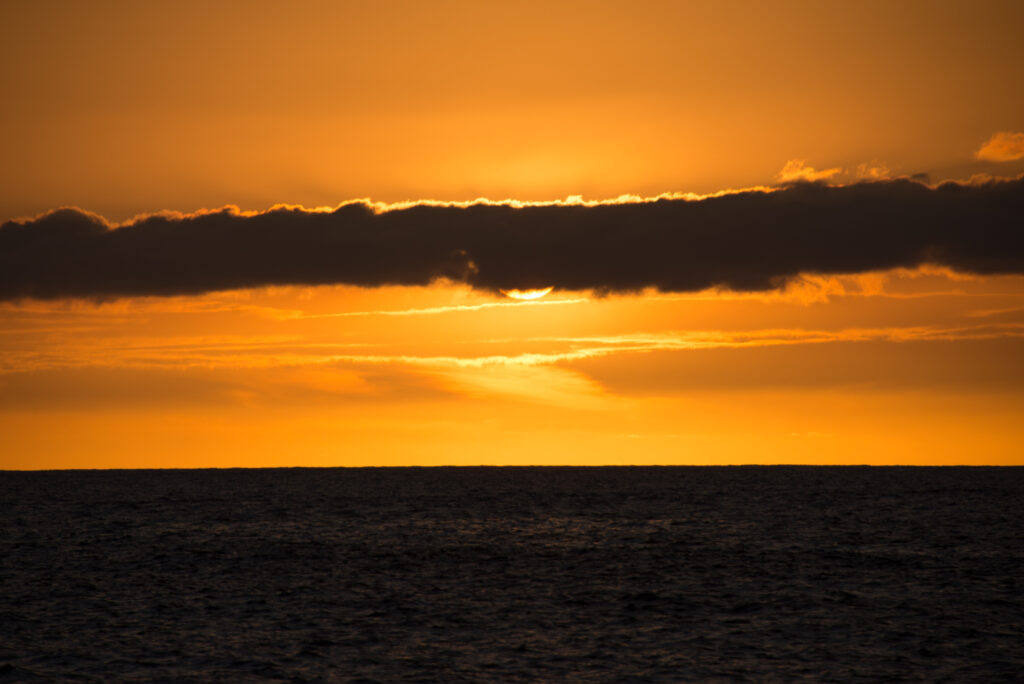 Sunset over calm sea with golden orange sky and dramatic cloud layer wallpaper background