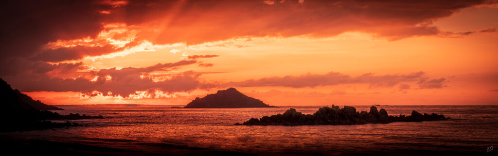 Sunset over ocean with island silhouette dramatic clouds and rugged sea rocks coastal wallpaper
