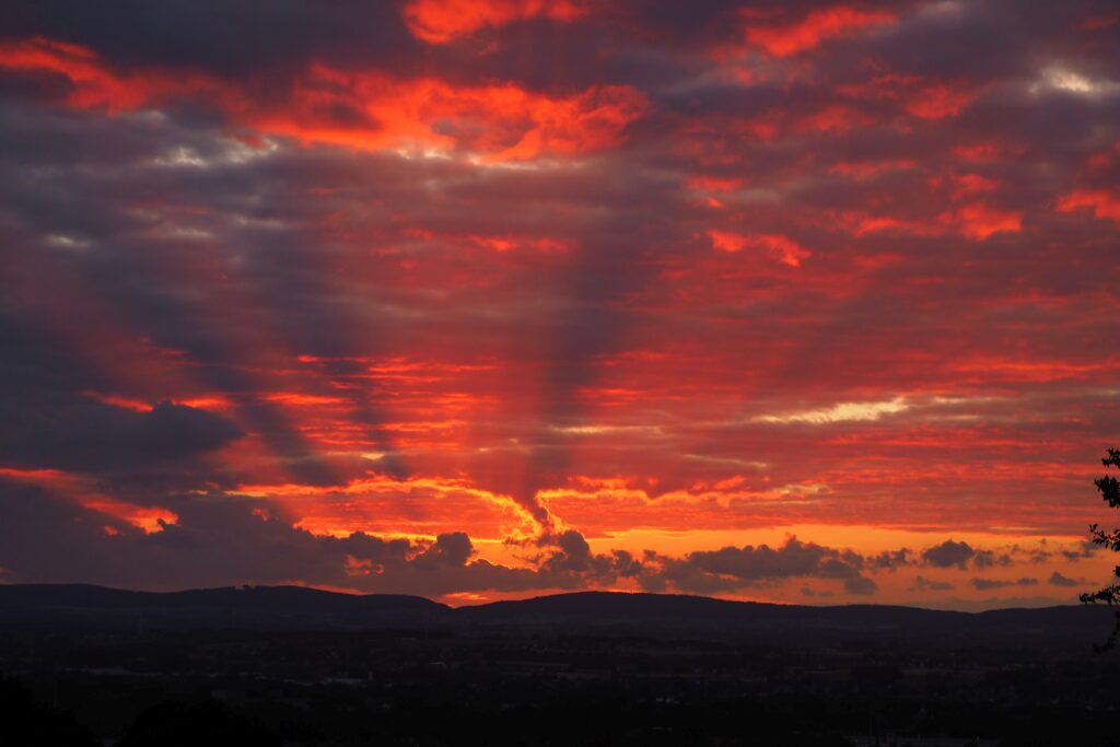 Sunset over rolling hills with vibrant orange red purple sky and dramatic sunlight rays wallpaper