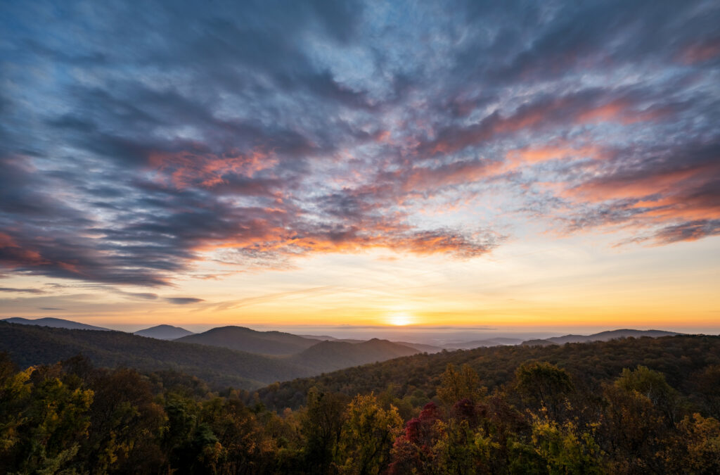 Sunset over rolling mountains with vibrant orange pink purple sky and forested hills wallpaper
