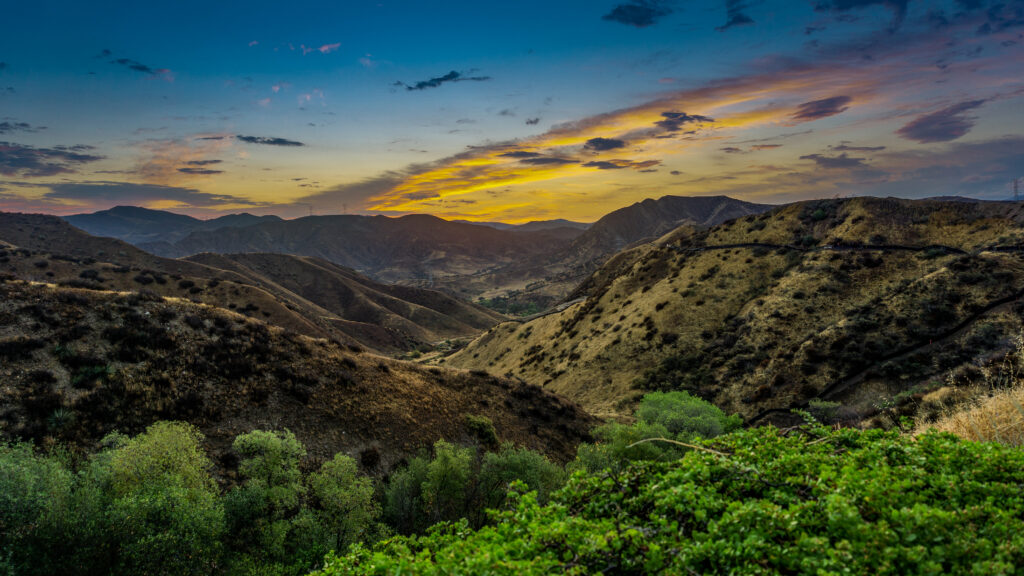 Breathtaking sunset over rugged mountains with golden light and lush green hills wallpaper background