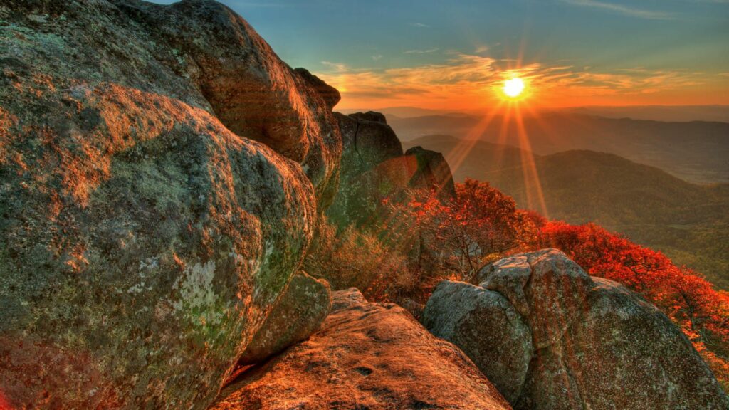 Breathtaking sunset over rugged stone formations with vibrant orange red foliage wallpaper background