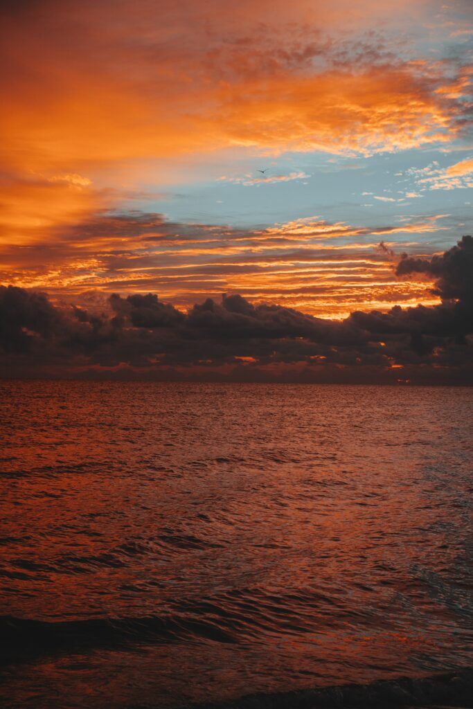 Sunset over calm sea with golden orange sky clouds reflecting on gentle rippling waves wallpaper