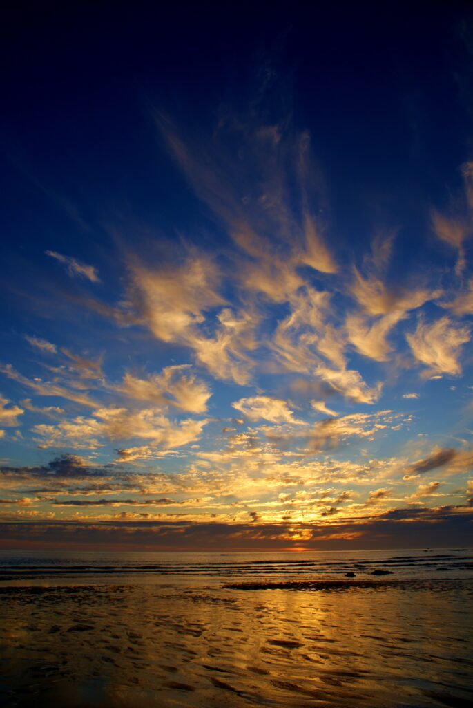 Sunset over calm sea with golden clouds reflecting on water and sandy horizon wallpaper background