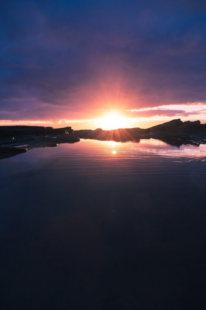 Sunset over tranquil lake with golden sun rays vibrant blue and purple sky serene landscape Wallpaper