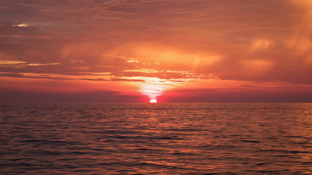 Sunset sea landscape wallpaper with warm glowing sun and vibrant orange red sky reflections