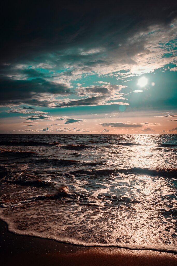 Sunset over ocean waves with golden light and dramatic clouds creating serene coastal view Wallpaper